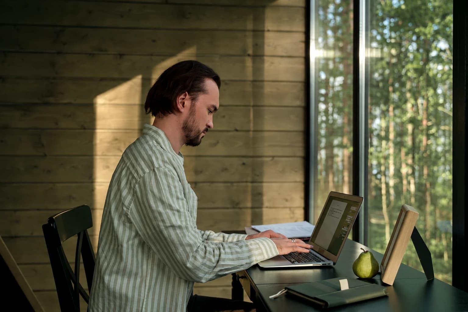 A man working on a laptop beside a window in a wooden room