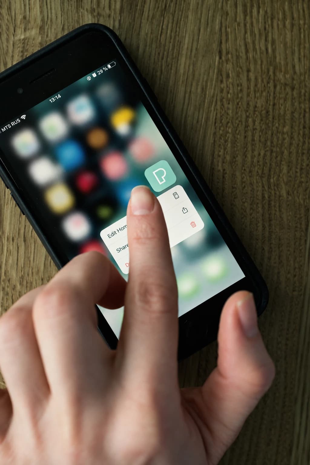 A hand using a smartphone on a wooden table
